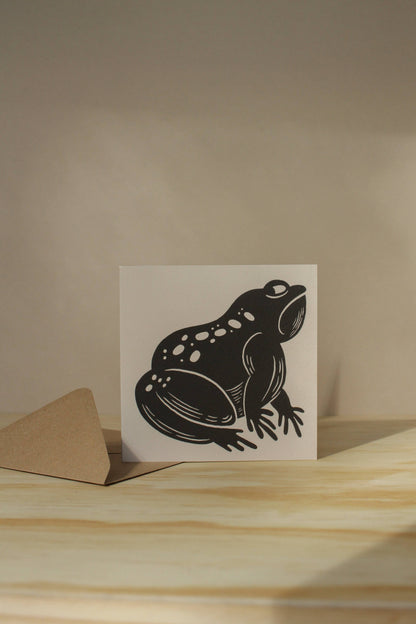 'The Grumpy Frog' card shown at an angle on its kraft envelope, part of Lauren Marina's square animal card series