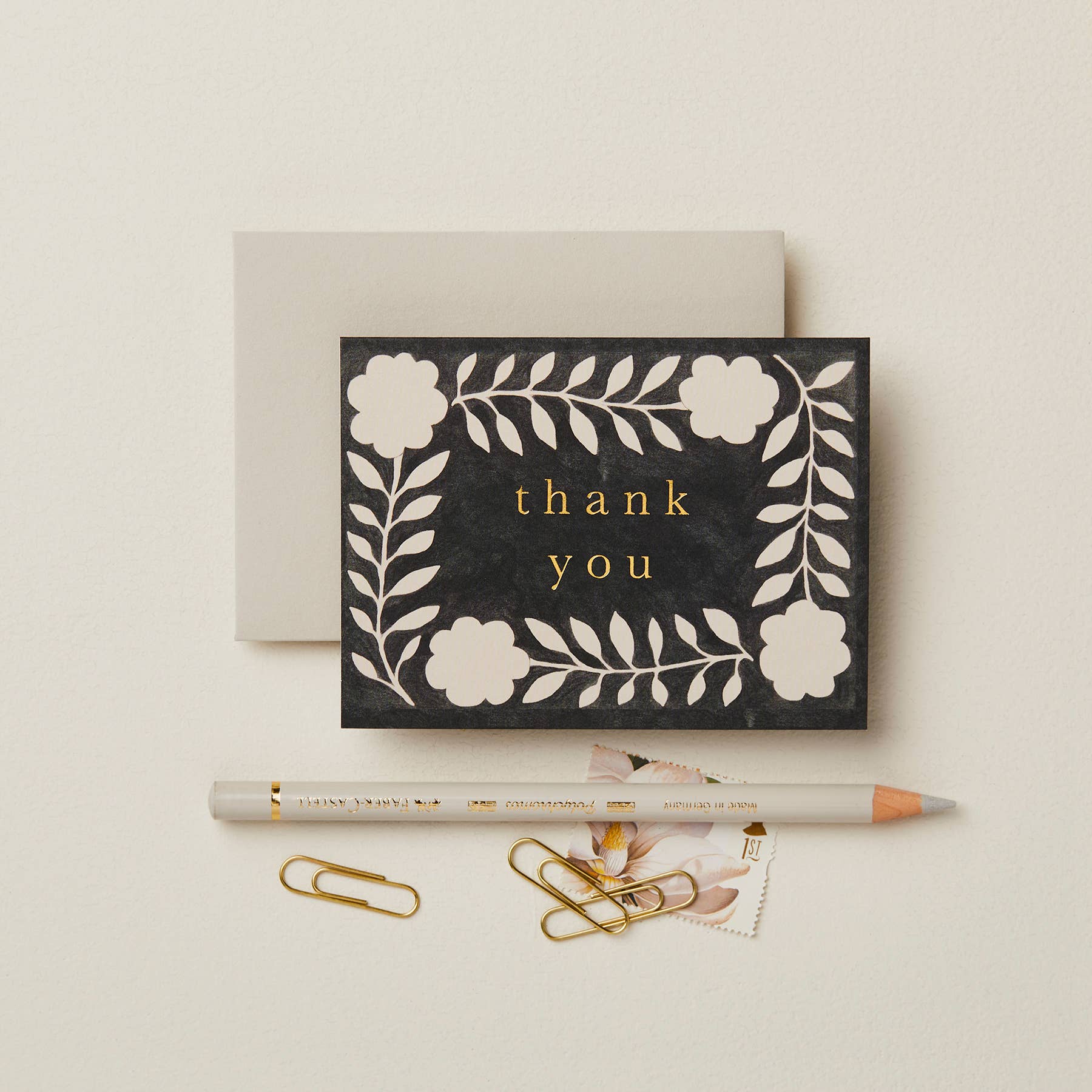 Black textured card with a cream floral wreath pattern, reading Thank You in gold script