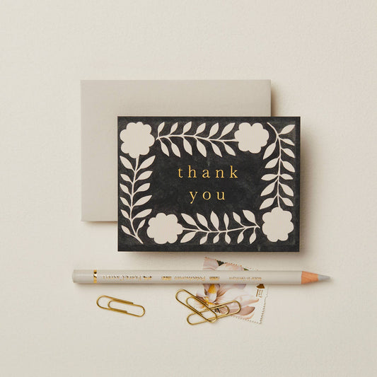 Black textured card with a cream floral wreath pattern, reading Thank You in gold script