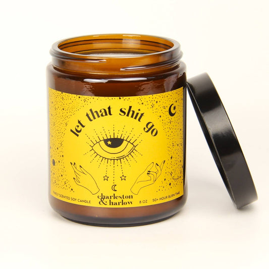 Charleston & Harlow Let That Shit Go soy candle in amber glass jar with mustard yellow label featuring a black mystic eye illustration