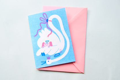 Angel & Swan Seasonal Risograph Card — illustration of a sleeping angel resting on a swan's back, shown on a pink envelope