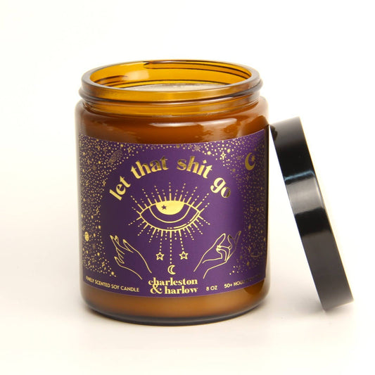 Charleston & Harlow Let That Shit Go soy candle in amber glass jar with purple label featuring a gold mystic eye and hands illustration