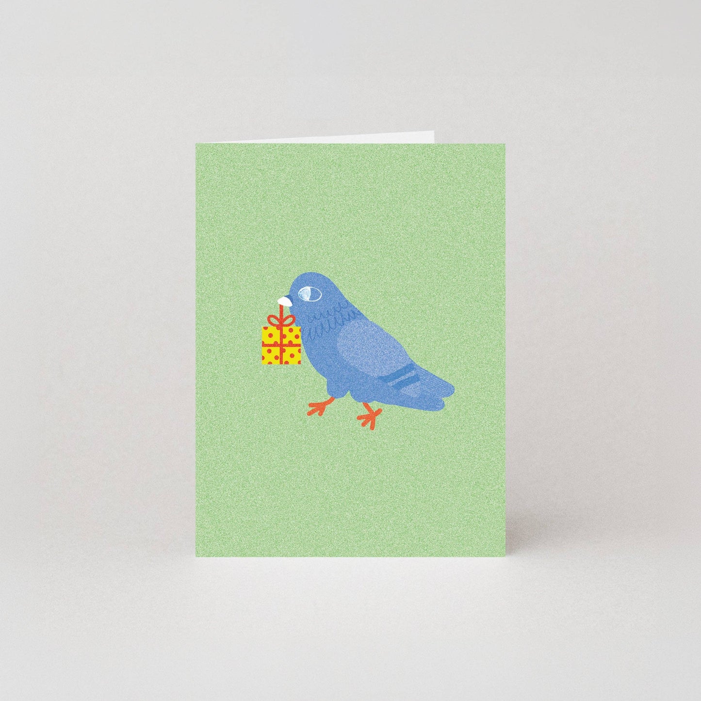 Mini birthday greeting card featuring an illustrated blue pigeon carrying a wrapped yellow gift box in its beak, on a sage green background.