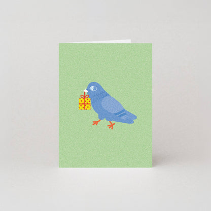 Mini birthday greeting card featuring an illustrated blue pigeon carrying a wrapped yellow gift box in its beak, on a sage green background.