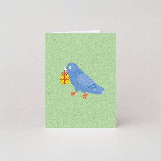 Mini birthday greeting card featuring an illustrated blue pigeon carrying a wrapped yellow gift box in its beak, on a sage green background.