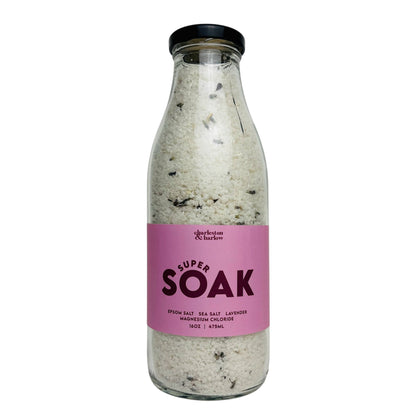 Glass bottle of Charleston & Harlow Super Soak bath salts with mauve label, magnesium and dried lavender buds visible in the salt