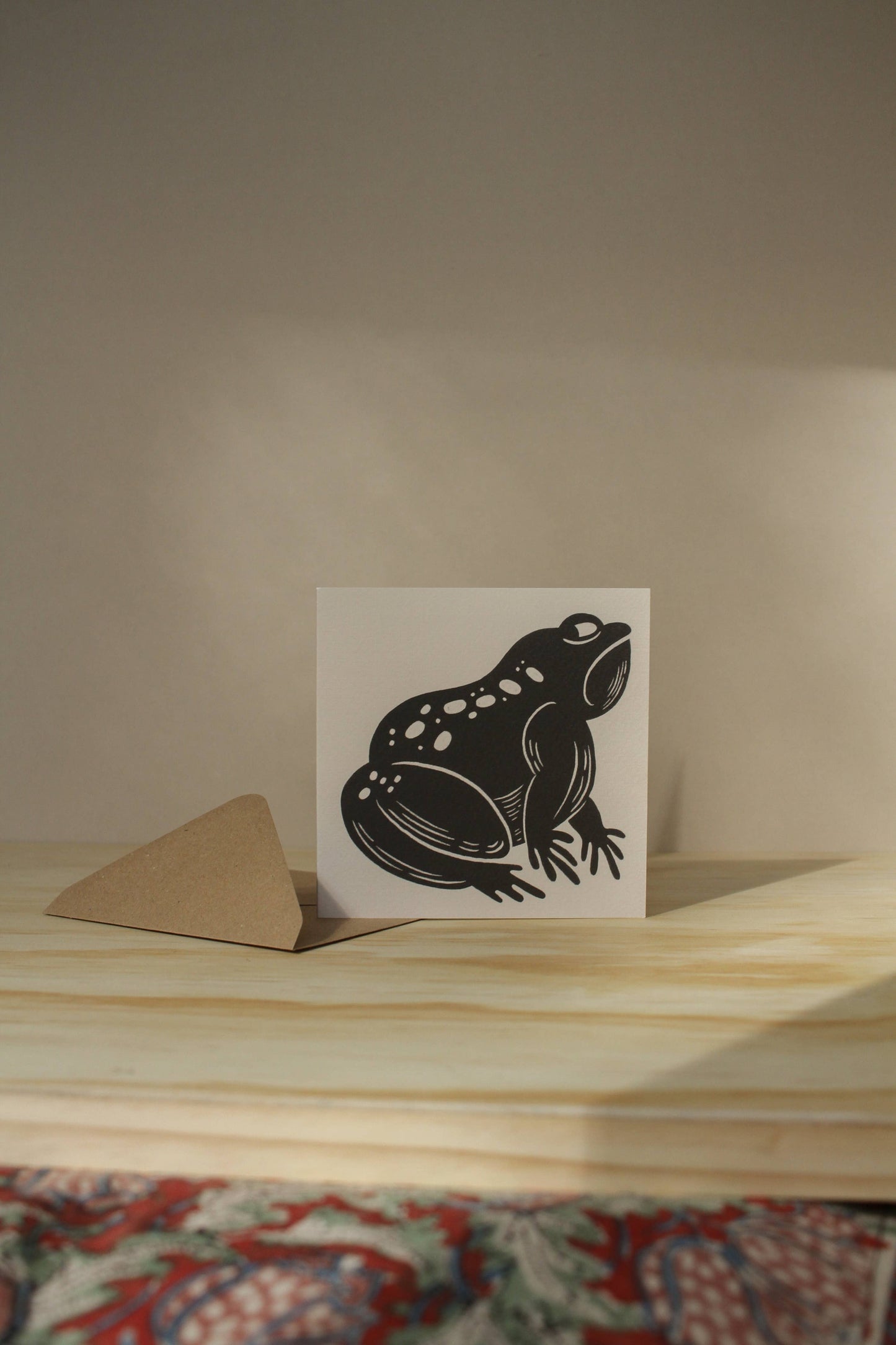 'The Grumpy Frog' card laid flat beside its kraft envelope on a light background