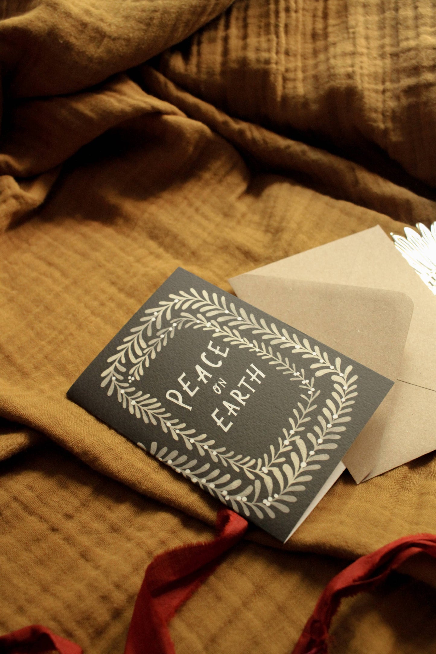 Close-up of the botanical wreath border illustration on the 'Peace on Earth' Christmas card