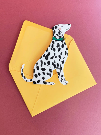 Kitty Kenda shaped sitting Dalmatian greeting card with a tiny gold bell, shown against a yellow envelope