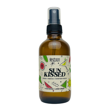Amber glass spray bottle of Charleston & Harlow Sun Kissed room and linen spray with colourful cream label featuring ocean and cocktail illustrations