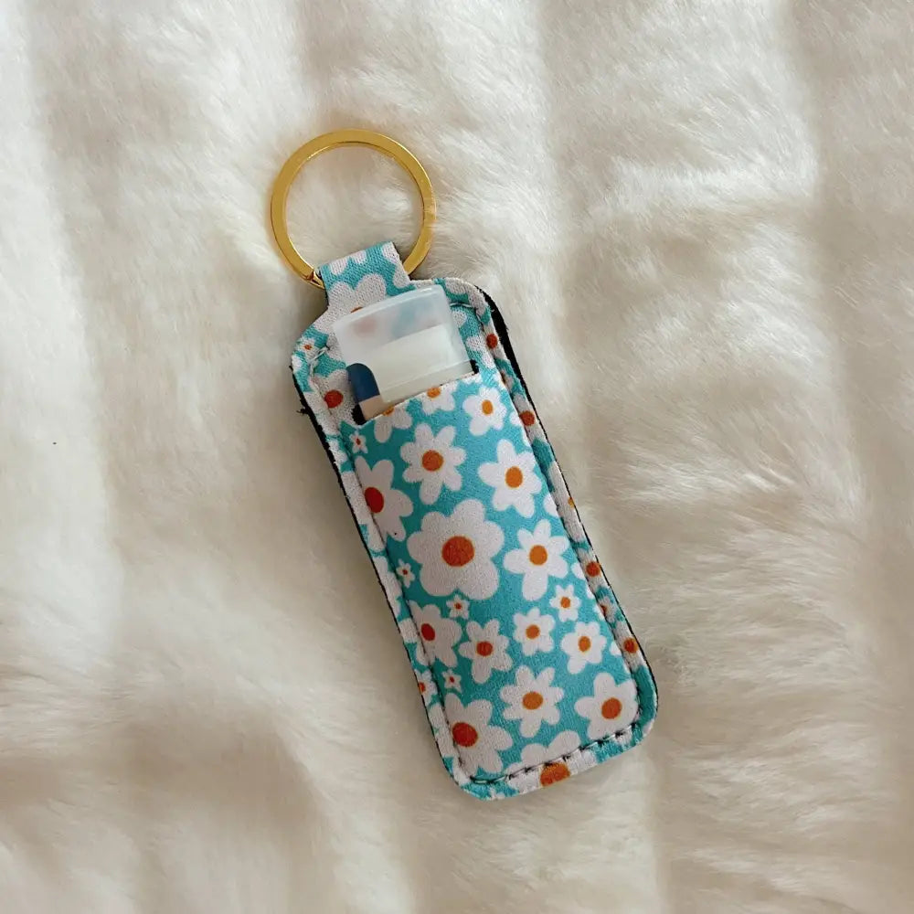 Blue floral lip balm holder with keyring, holding a standard lip balm tube, displayed on soft white fur.