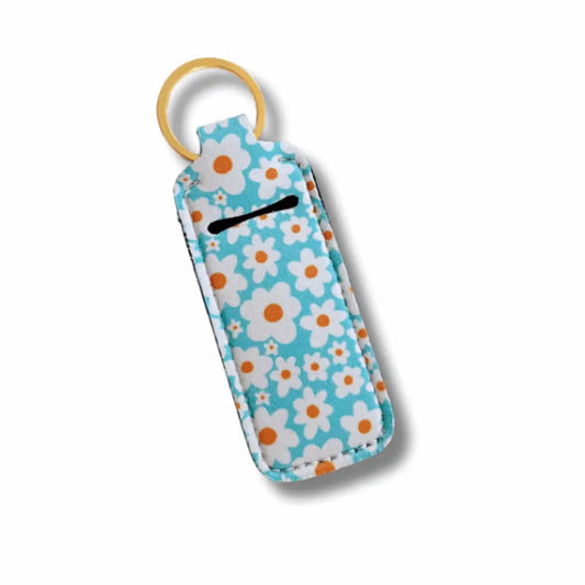 Blue daisy-print neoprene lip balm holder with gold keyring and stitched edges, shown flat against a white background.