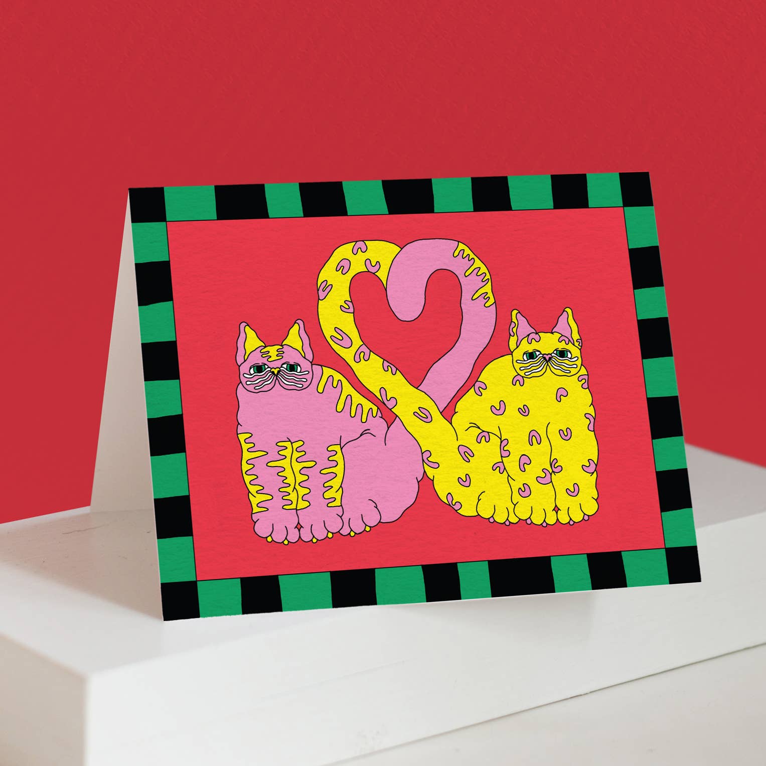 Pink and yellow spotted cats forming a heart shape with their tails, on red background with green and black checkered border
