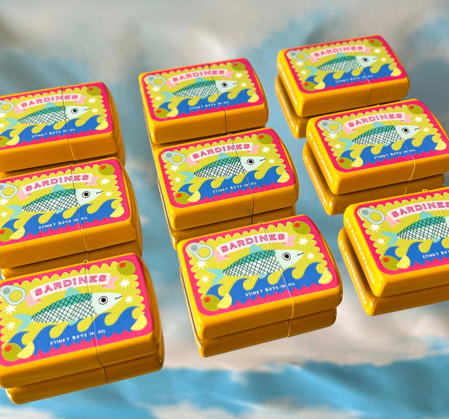 Gold metal lighter printed with a vintage sardine tin illustration reading Sardines, Stinky Boys In Oil