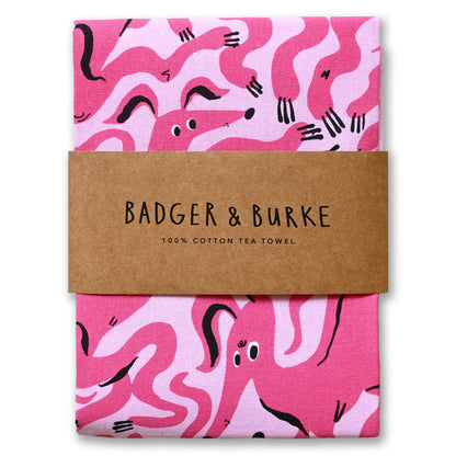 Folded pink cotton tea towel printed with wiggly hot pink dogs, Badger + Burke kraft band - PABOOM