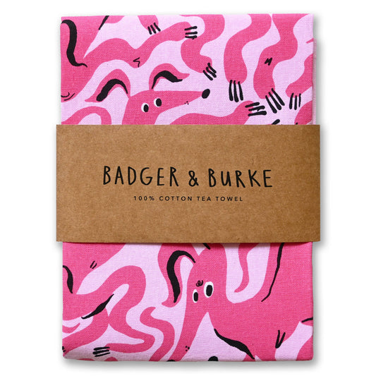 Folded pink cotton tea towel printed with wiggly hot pink dogs, Badger + Burke kraft band - PABOOM