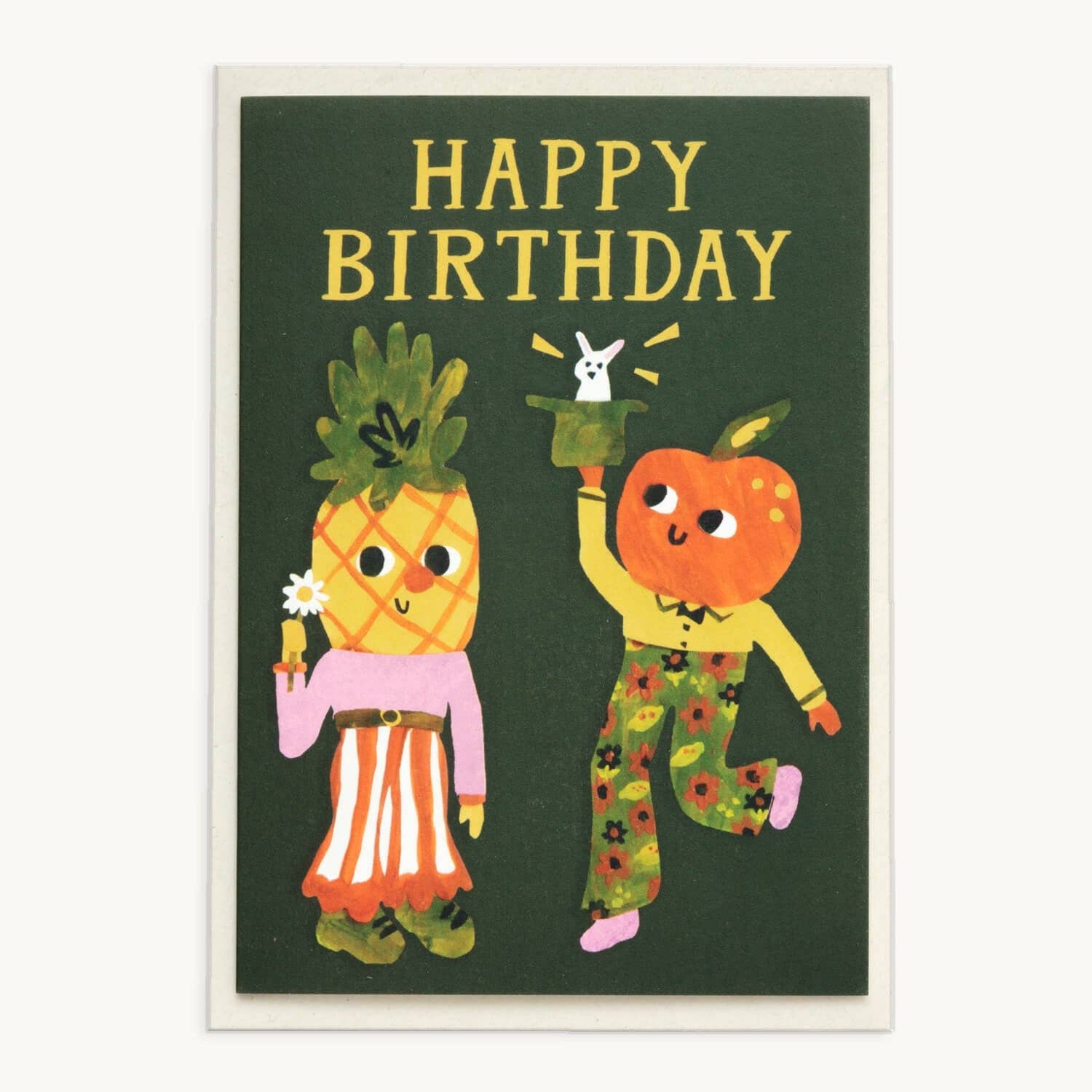 Dark green greeting card reading 'Happy Birthday' in gold, with an illustrated pineapple character holding a flower and an orange character pulling a rabbit from a top hat