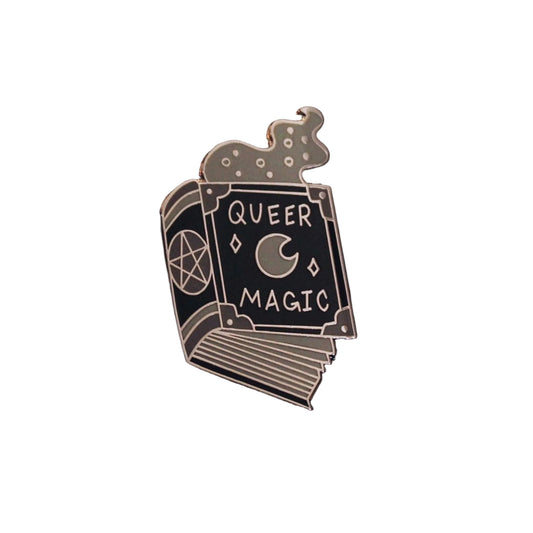Silver-plated enamel pin shaped like a spellbook with a pentacle and crescent moon, reading Queer Magic, with smoke swirling from the pages
