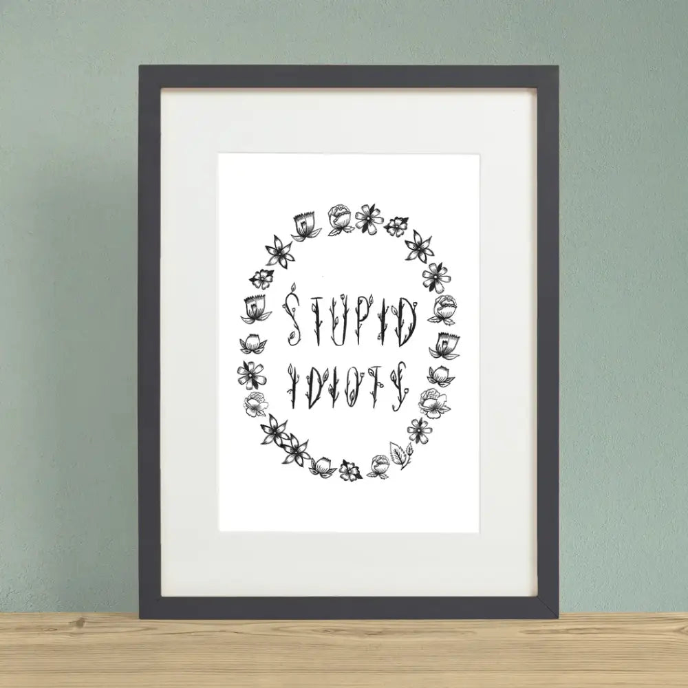 Floral black font saying STUPID IDIOTS surrounded by flower outlines on a white background print in black frame - PABOOM