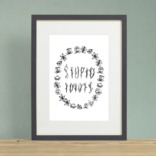 Floral black font saying STUPID IDIOTS surrounded by flower outlines on a white background print in black frame - PABOOM