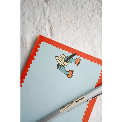 Notepad with a top logo of two hands writing a letter “SUP BABE”. Blue, with red squiggle outline by Stay Home Club | PABOOM