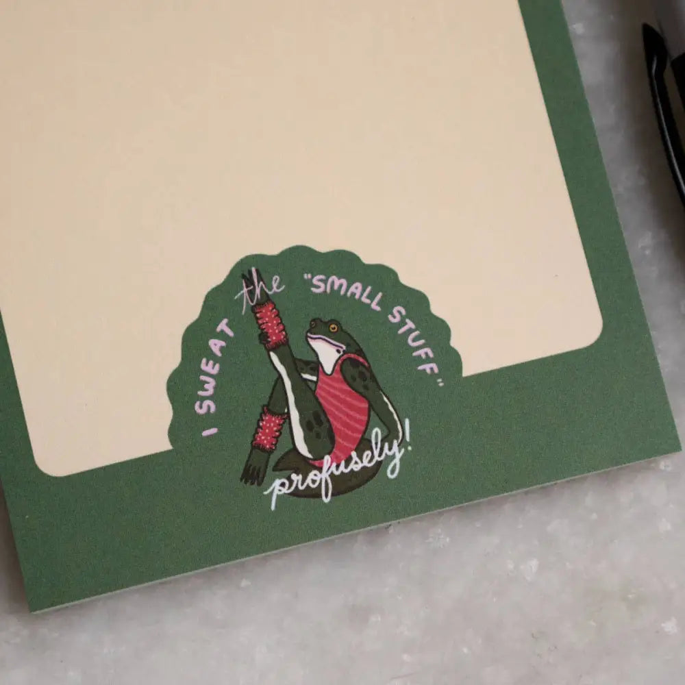 Notepad with a logo of a frog doing aerobics and text “I SWEAT THE SMALL STUFF … profusely” by Stay Home Club, close up - PABOOM