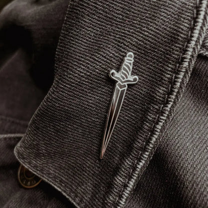 a dagger shaped pin on a black jean jacket