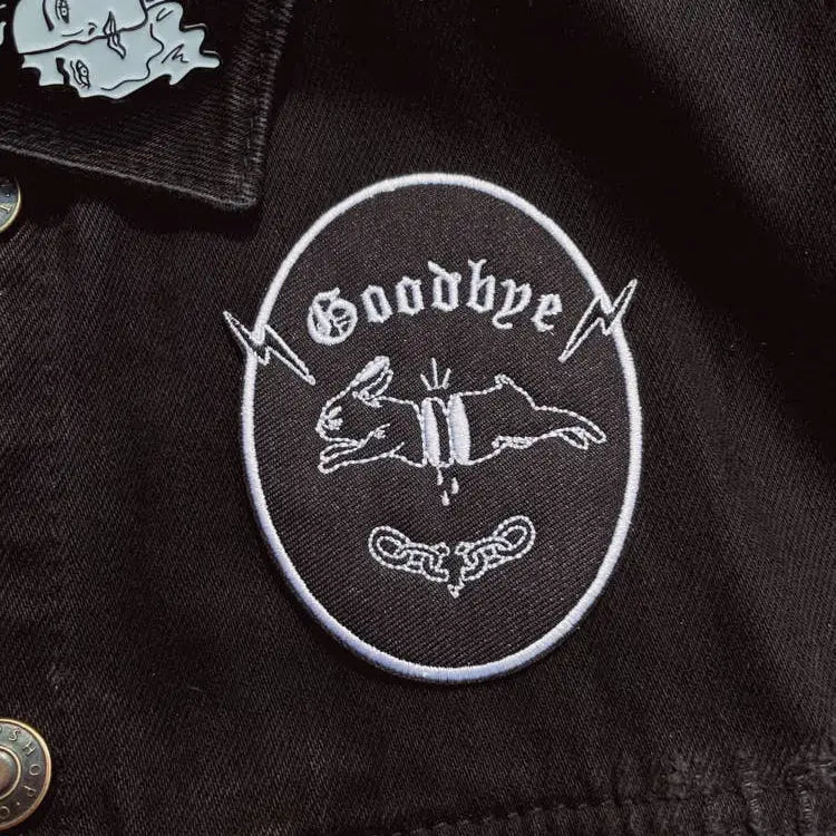 Iron on embroidered patch of a chopped-up rabbit jumping and "goodbye" written underneath, Black with white embroidery, on fabric