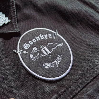 Iron on embroidered patch of a chopped-up rabbit jumping and "goodbye" written underneath. Black with white embroidery. on fabric