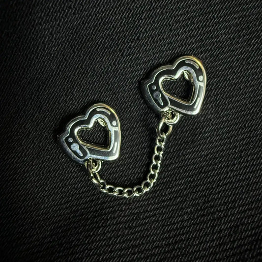 A pair of heart handcuffs enamel pin on black fabric