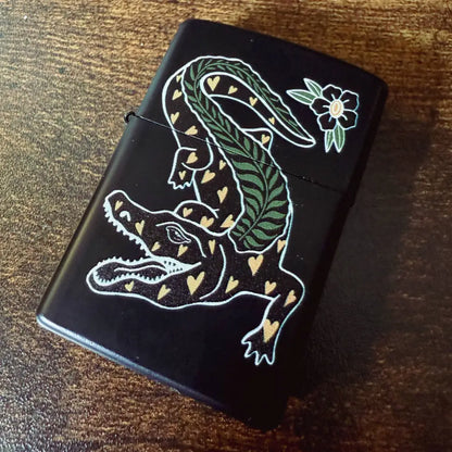 Zippo black lighter with a decorative heart and fern pattered alligator on wood background