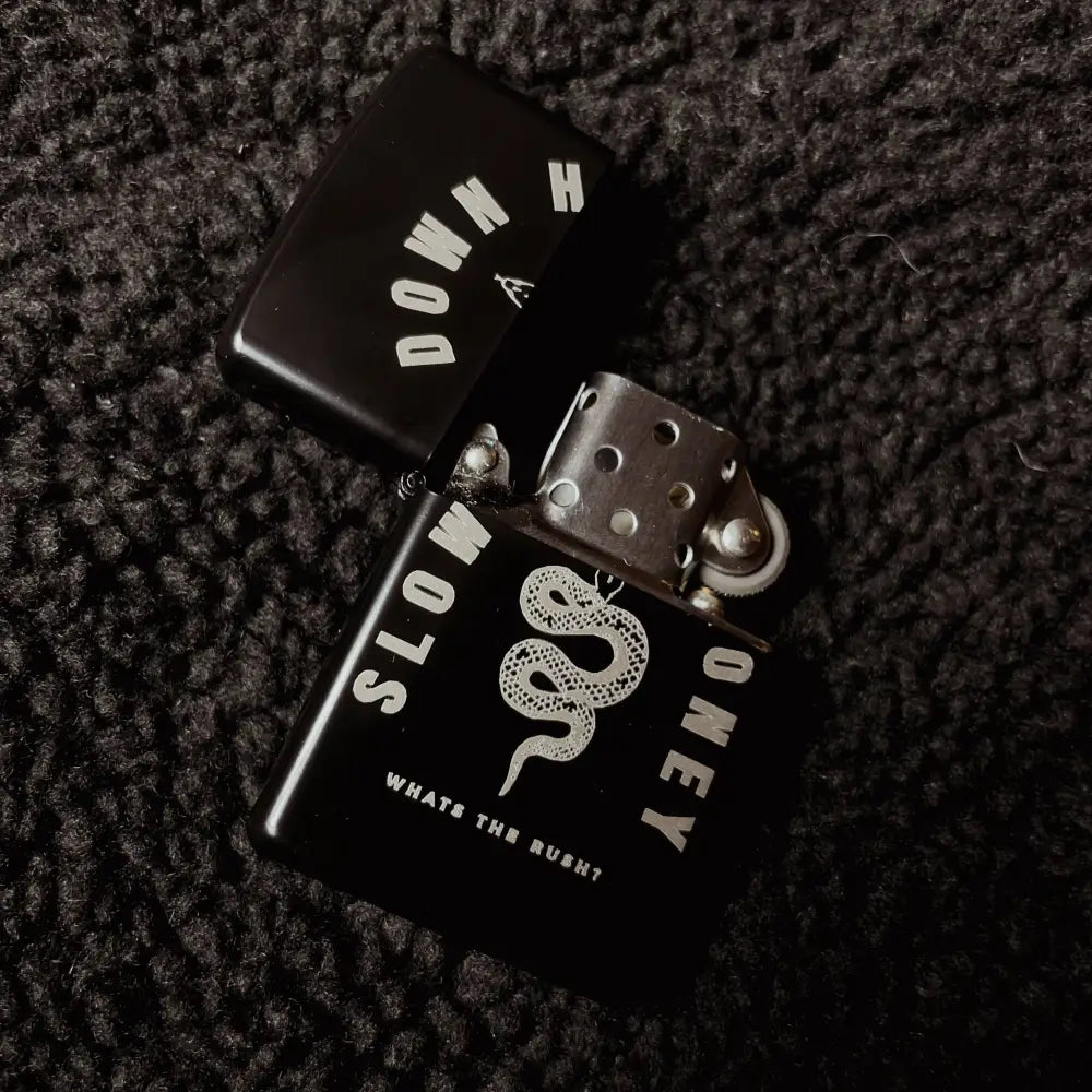 Zippo black lighter with a snake and text SLOW DOWN HONEY whats the rush?, opened on black fabric
