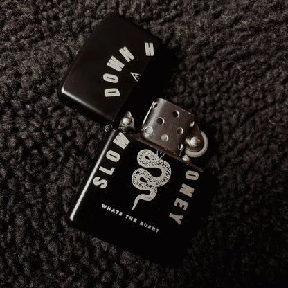 Zippo black lighter with a snake and text SLOW DOWN HONEY whats the rush?, opened on black fabric